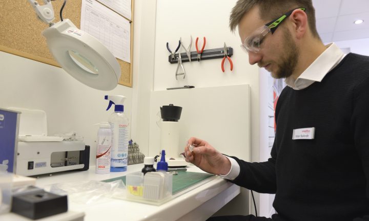 Ein Auszubildender zum Hörakustiker bereitet ein Hörgerät vor.