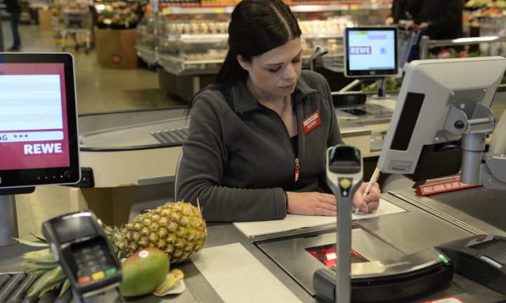 Eine Auszubildende zur Einzelhandelskauffrau sitzt im Supermarkt an der Kasse.