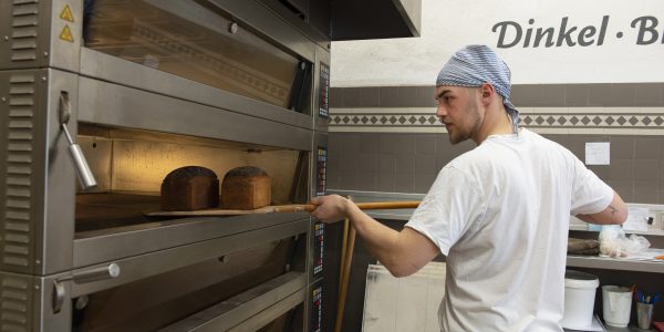 Ein Bäckerazubi schiebt Brot in den Ofen.