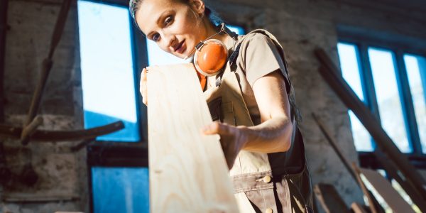 Eine junge Zimmerin überprüft in der Werkstatt die Qualität eines Brettes.