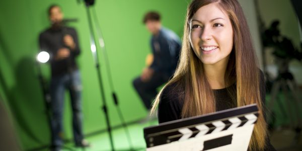 Eine junge Frau hält in einem Studio mit Greenscreen die Filmklappe.