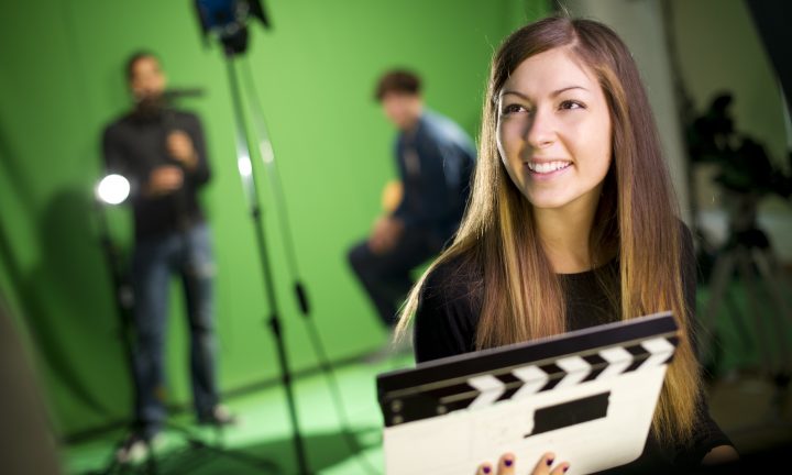 Eine junge Frau hält in einem Studio mit Greenscreen die Filmklappe.