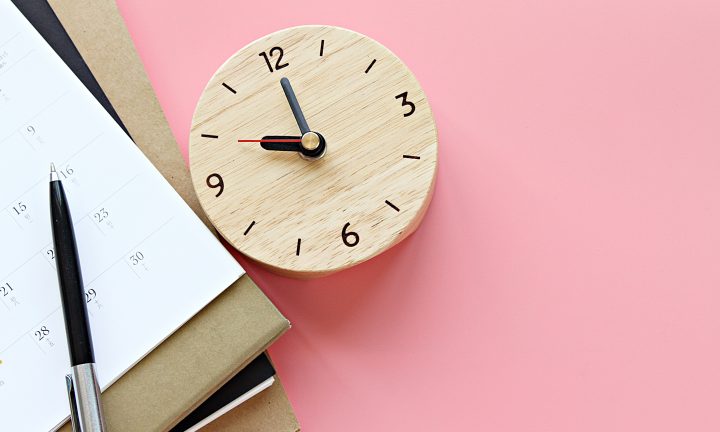 Auf einem Tisch liegen ein Kalender, Notizbücher, ein Stift und eine Uhr.