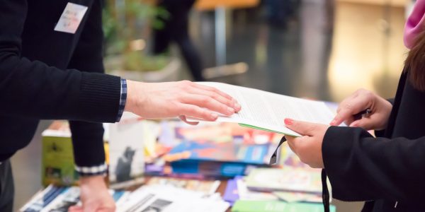 Ein Mann und eine Frau reichen ein Informationsblatt über den Messestand.