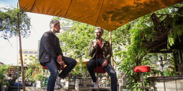 zwei Männer sitzen auf der Bühne und tauschen sich aus