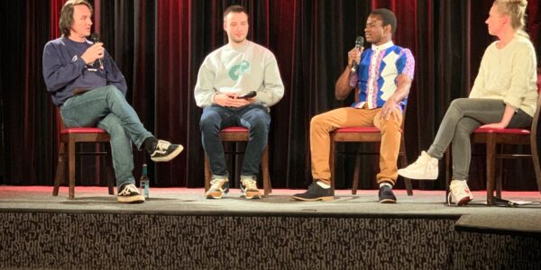 vier Menschen sitzen auf einer Bühne, zwei sprechen in ein Mikrofon