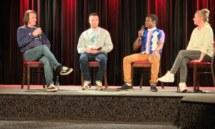 vier Menschen sitzen auf einer Bühne, zwei sprechen in ein Mikrofon
