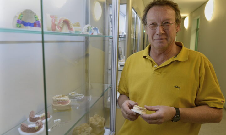 Zahntechniker hält ein Gipsmodell mit kunstfertig modellierten Ersatzzähnen und Metallverbindungen in der Hand