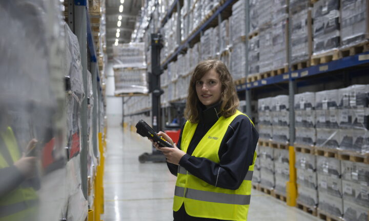 Kauffrau für Spedition und Logistikleistungen steht in Lagerhalle und scannt Ware.