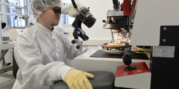 Auszubildender zum Mikrotechnologen in weißer Arbeitskleidung schaut durch Mikroskop