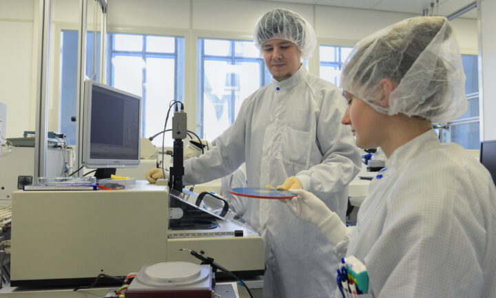 Ein Auszubildender zum Mikrotechnologen und eine Auszubildende zur Mikrotechnologin arbeiten an Maschine