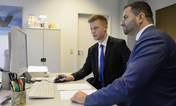 Auszubildender zum Fachwirt für Versicherungen und Finanzen bei der Debeka LGS Berlin schaut mit Chef auf einen Desktop.