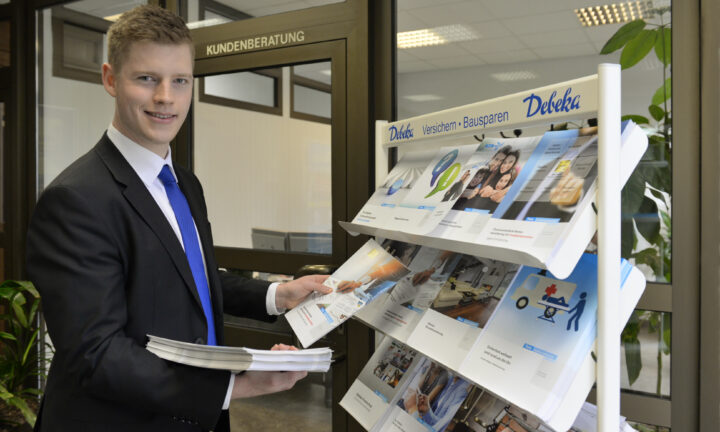 Auszubildender zum Fachwirt für Versicherungen und Finanzen sortiert Versicherungshefte in eine Infotheke ein.