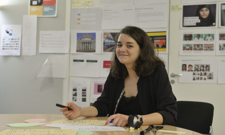 Junge Frau sitzt vor Pinnwänden im Büro und beschriftet Karten.