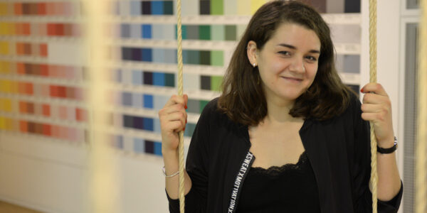 Junge Frau sitzt auf Schaukel in einem Büro und lächelt in Kamera.