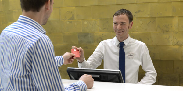 Hotelfachmann reicht Kunden seine Zimmerkarte über den Tresen.
