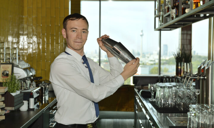 Hotelfachmann steht an der Bar und mischt ein Getränk.