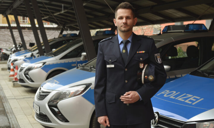 Junger Mann in Polizeiuniform steht vor parkenden Polizeiautos