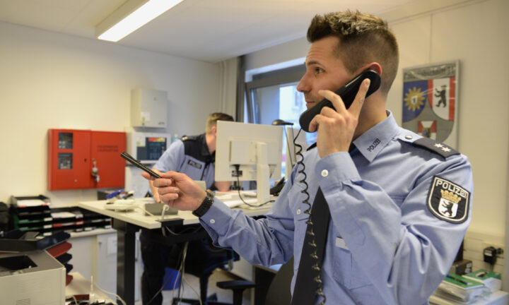 Polizist steht im Büro und spricht in einen Telefonhörer.