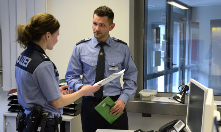 Polizisten und Polizist stehen im Büro und schauen in eine Akte.