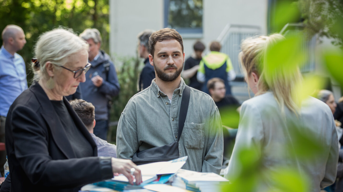 drei Personen sind im Gespräch, in der Mitte ein junger Mann
