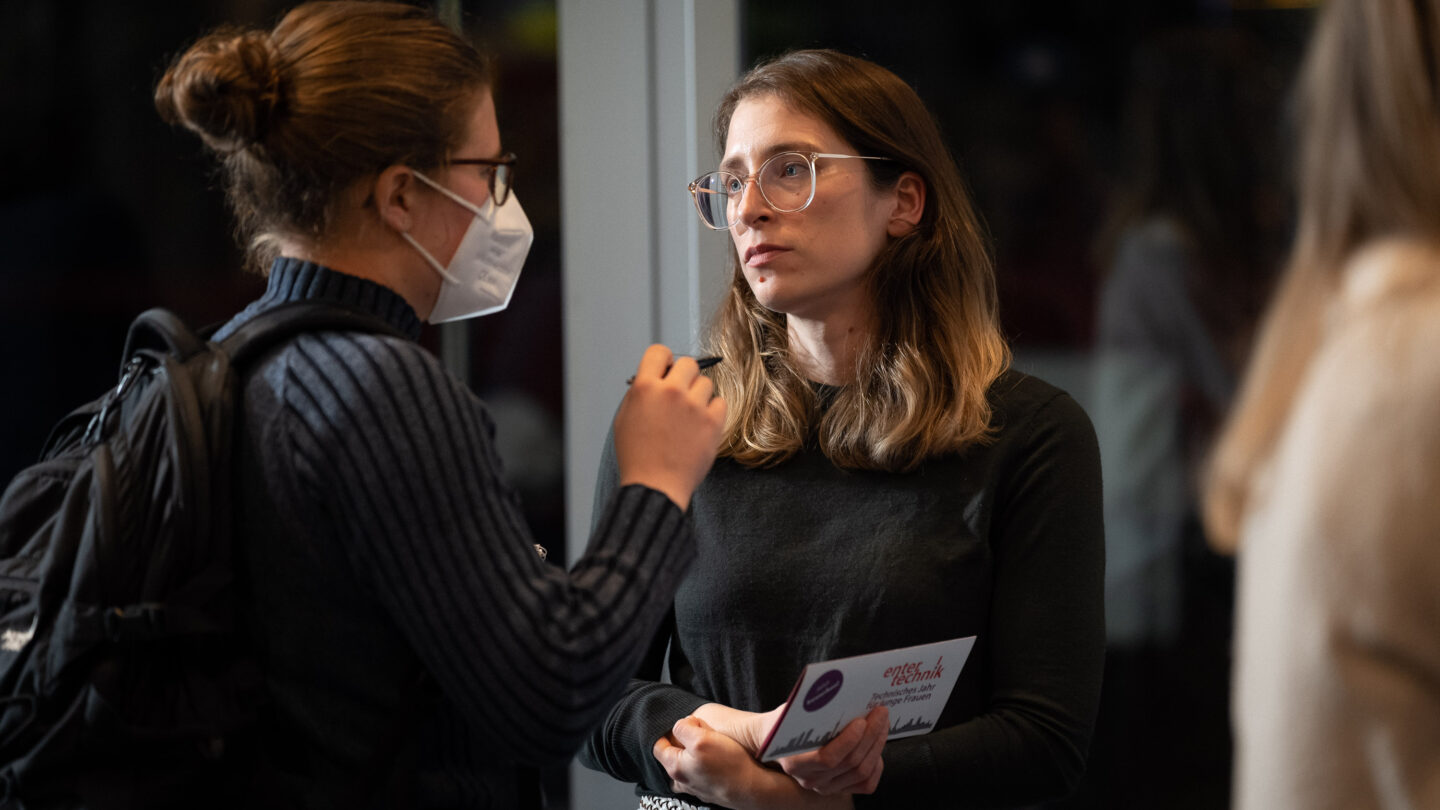 Zwei Frauen unterhalten sich. Die linke Frau trägt eine Maske.