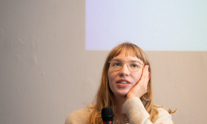 Eine junge Frau sitzt auf der Bühne und spricht ins Mikrofon
