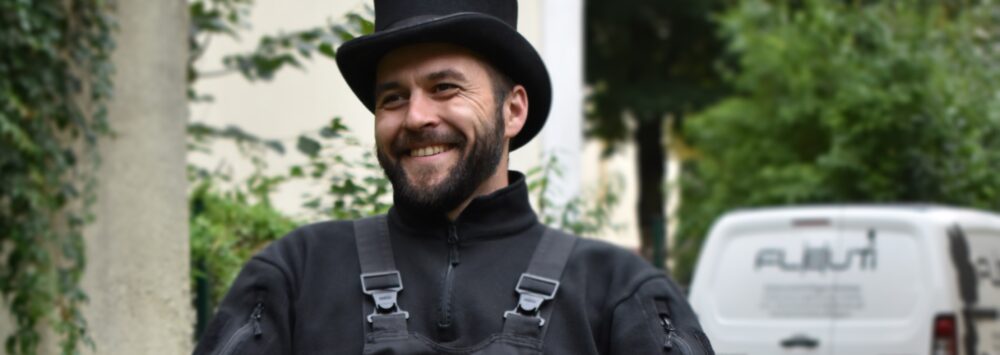 Der Schornsteinfeger Philipp Fleuti sitzt auf einem Stuhl im Hinterhof seines Berliner Büros und berichtet von seinem Studienabbruch sowie weiteren beruflichen Werdegang.