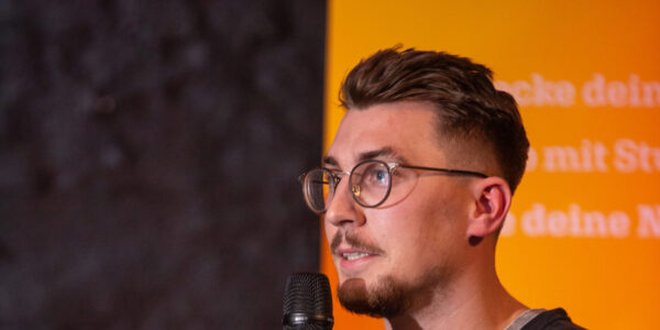Junger Mann auf der Bühne spricht in das Mikrofon.