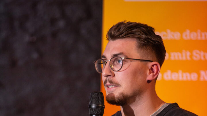 Junger Mann auf der Bühne spricht in das Mikrofon.