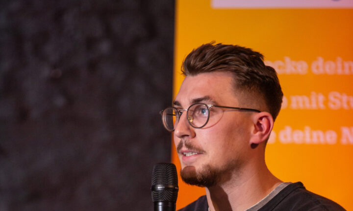 Junger Mann auf der Bühne spricht in das Mikrofon.