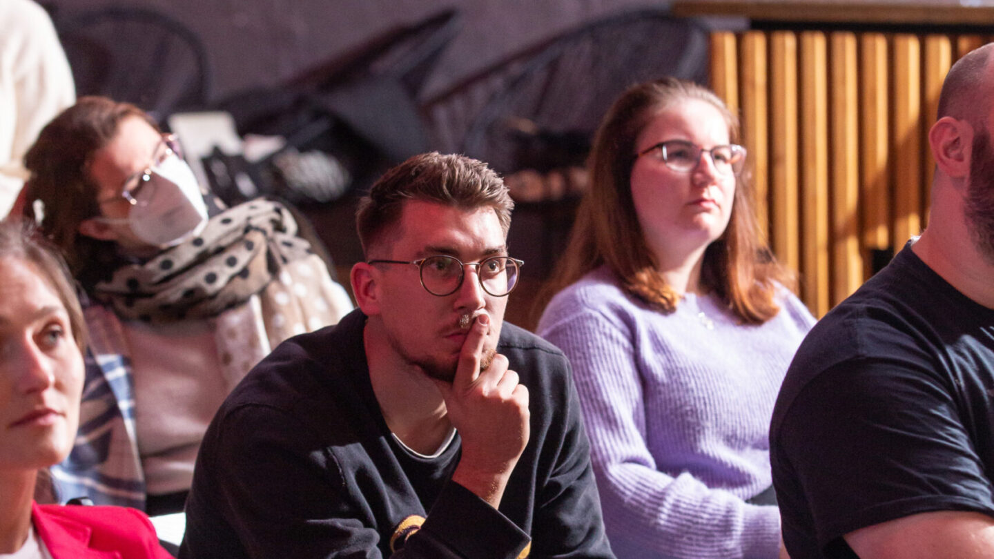 Fünf Personen im Publikum. Ein junger Mann ist im Fokus und schaut nachdenklich.