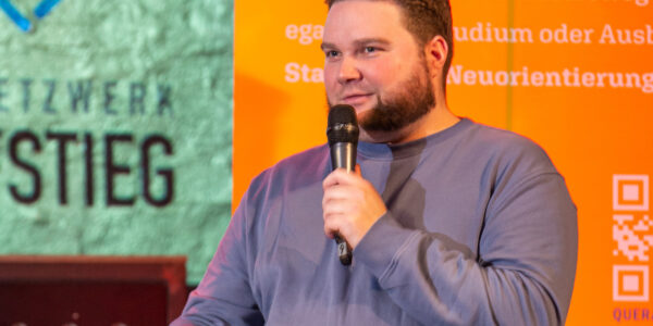 Ein junger Mann sitzt auf der Bühne und spricht in das Mikrofon.