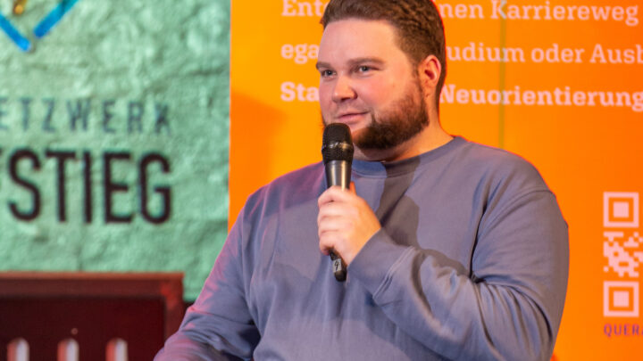 Ein junger Mann sitzt auf der Bühne und spricht in das Mikrofon.