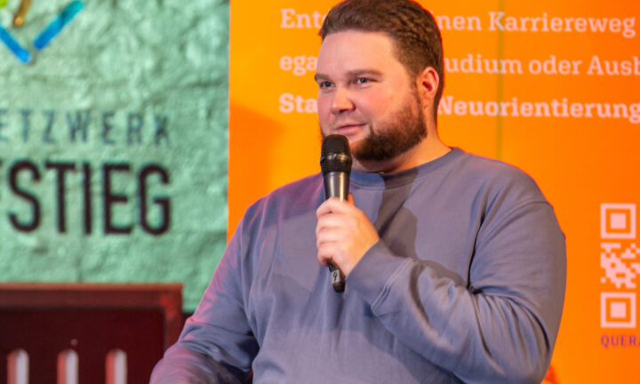 Ein junger Mann sitzt auf der Bühne und spricht in das Mikrofon.