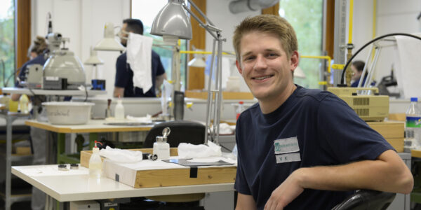 Ein junger Mann in der Werkstatt lacht in die Kamera