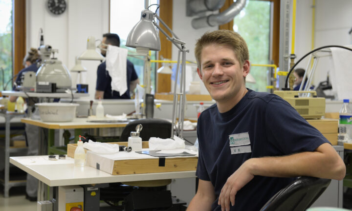 Ein junger Mann in der Werkstatt lacht in die Kamera