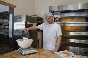 Der Bäckerazubi misst Mehl auf einer Waage ab.