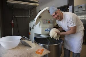 Ein Bäckerazubi mit Teig in der Hand steht vor der Mehlmaschine