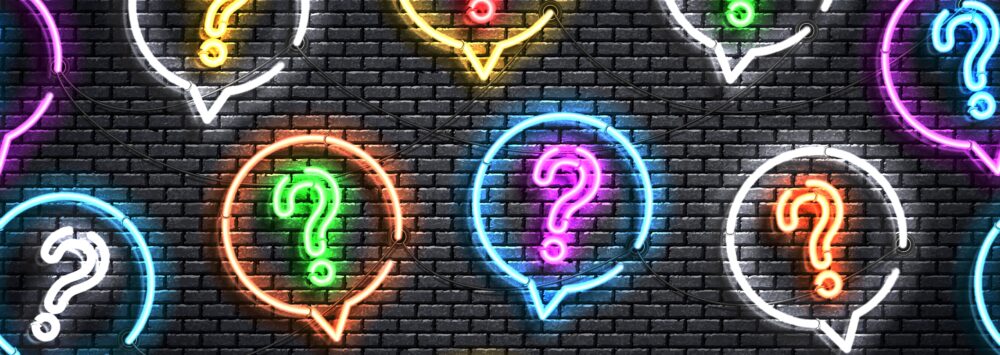 Bunte Neonröhren in Form von Fragezeichen vor einer grauen Mauer