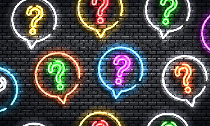 Bunte Neonröhren in Form von Fragezeichen vor einer grauen Mauer