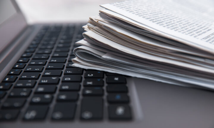 Ein Stapel Tageszeitungen liegt auf der Tastatur eines Laptops.