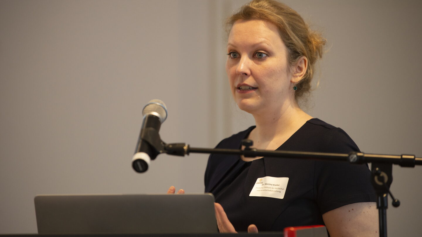 Eine Frau steht an einem Rednerpult und hält eine Präsentation