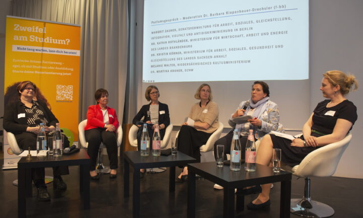 Sechs Frauen sitzen auf Stühlen auf einer Bühne und moderieren eine Gesprächsrunde