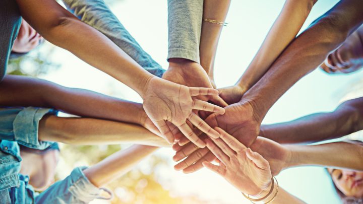 Eine Gruppe verschiedener Menschen legt die Hände übereinander.