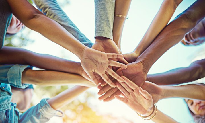 Eine Gruppe verschiedener Menschen legt die Hände übereinander.