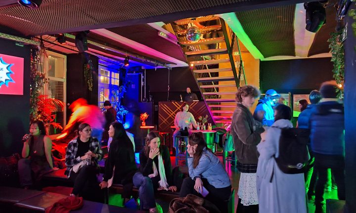 Mehrere junge Menschen unterhalten sich angeregt in einem bunt beleuchteten Nachtclub.