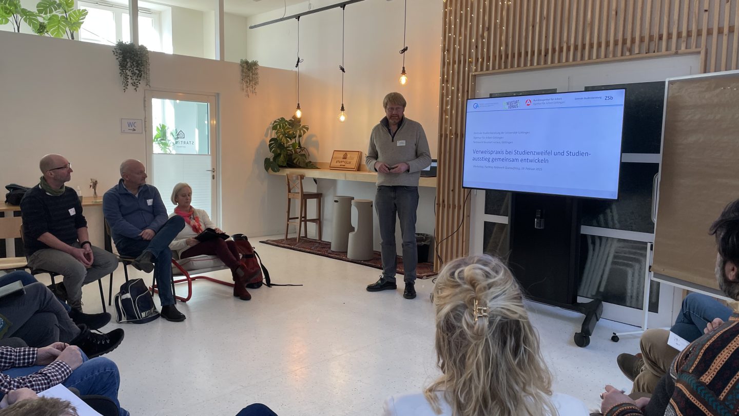 Ein Mann präsentiert auf einem Bildschirm seinen Input vor einem kleinen Publikum, das im Halbkreis um ihn herumsitzt.