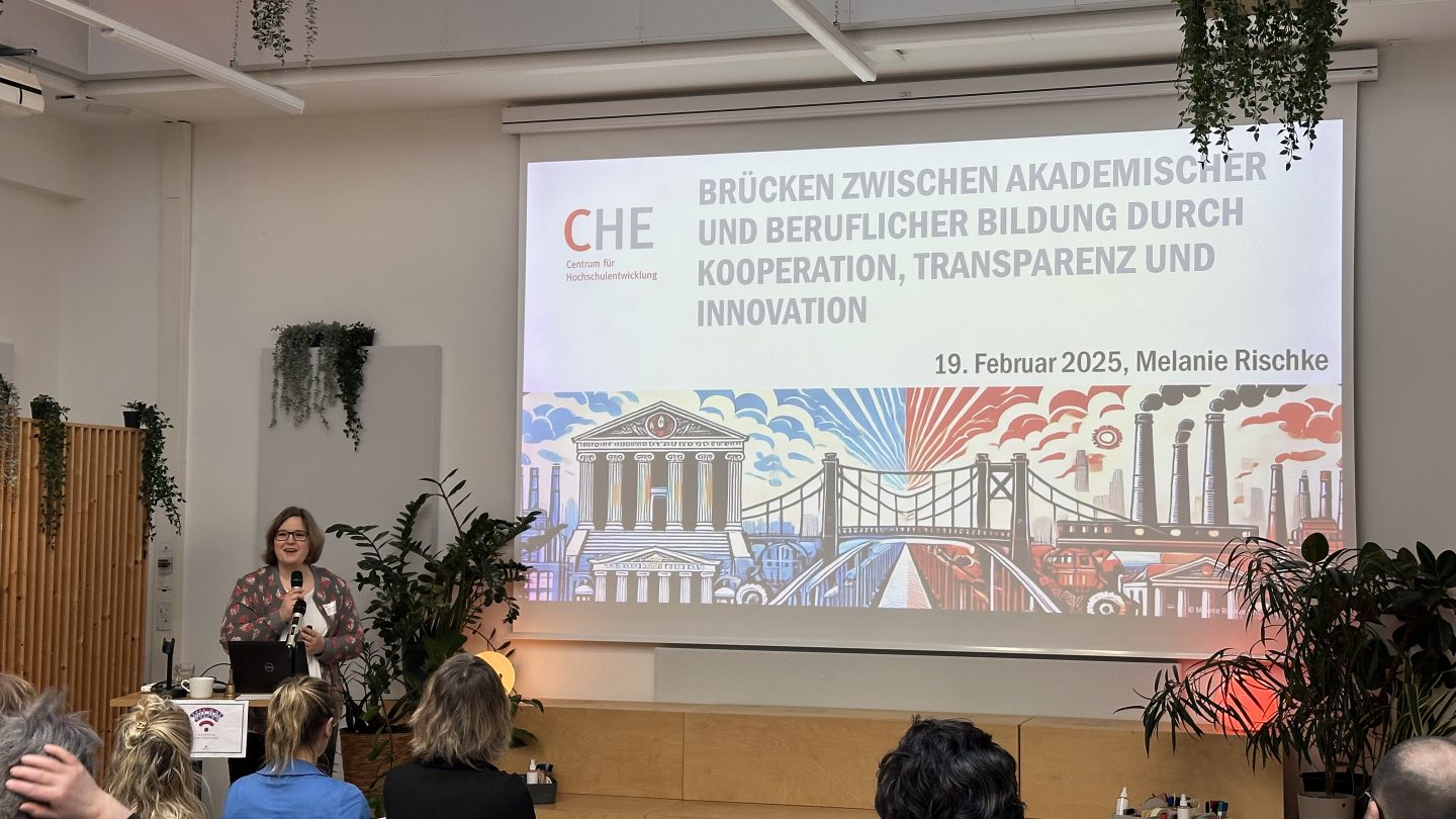 Eine Frau steht am Rednerpult vor einer Präsentation und spricht zum Publikum.