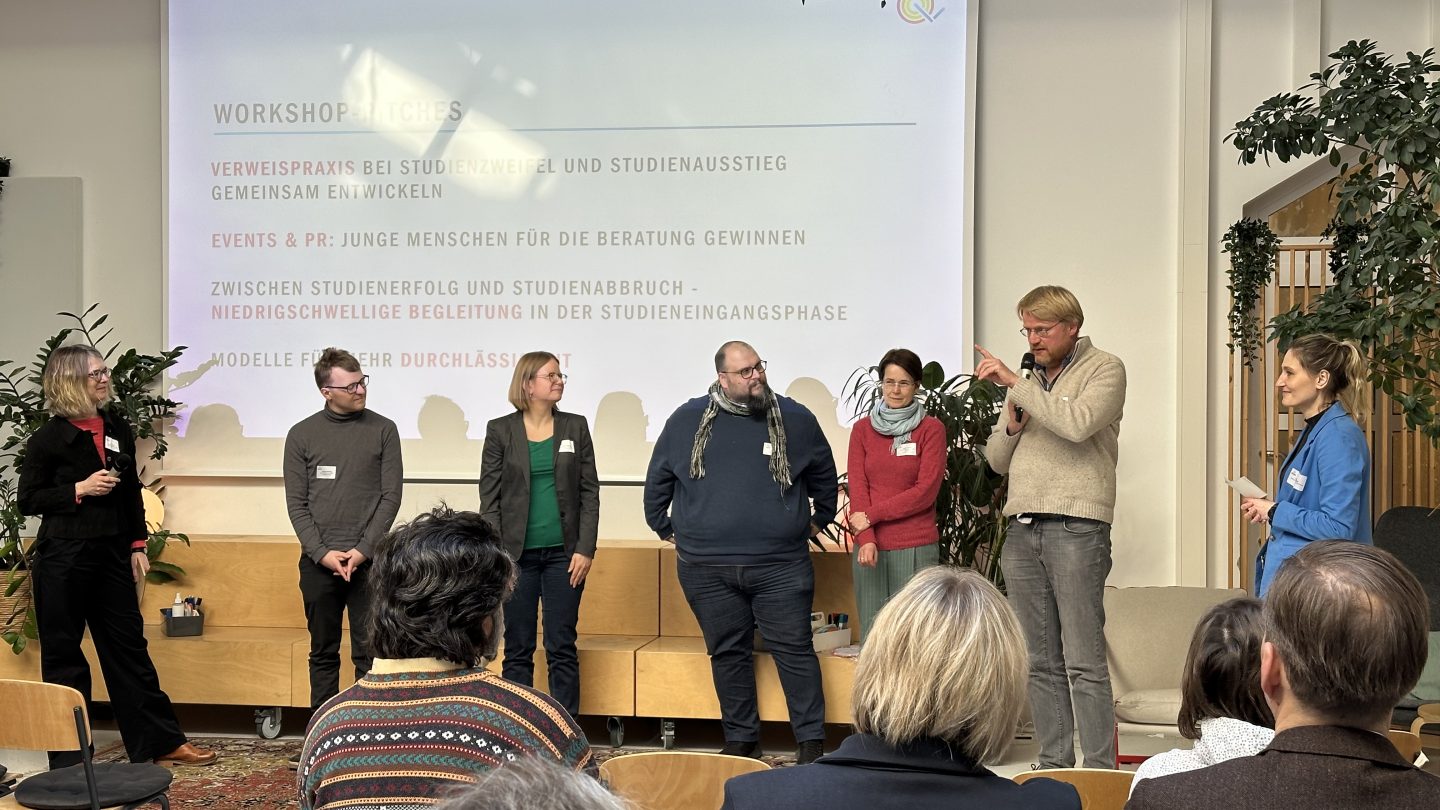 Fünf Männer und Frauen stehen zusammen mit zwei Moderatorinnen auf der Bühne und sprechen nacheinander zum Publikum.